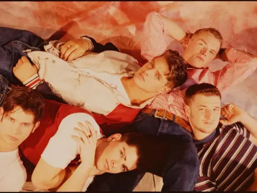 Medlemmar av Boyzone ligger tätt tillsammans, klädda i jeans och färgglada toppar.