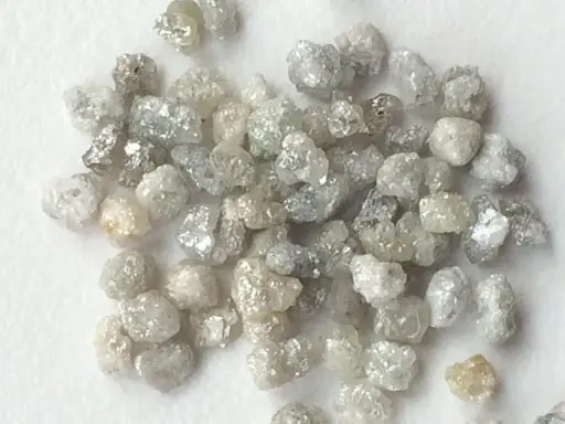 Un mucchio di grezzi diamanti non lavorati, con sfumature che vanno dal bianco al grigio e un leggero tocco dorato, pronti per essere trasformati.