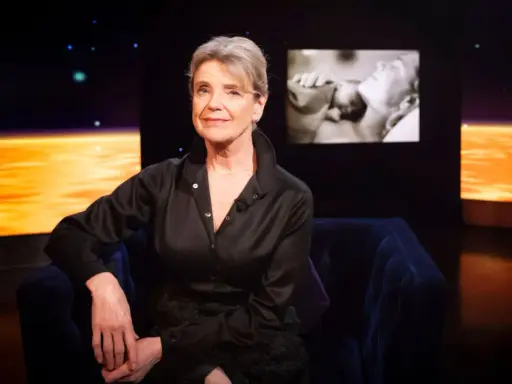 Stina Ekblad sitter i en mörkblå soffa, med en skärm bakom sig som visar klipp från filmer och tv-program med henne.