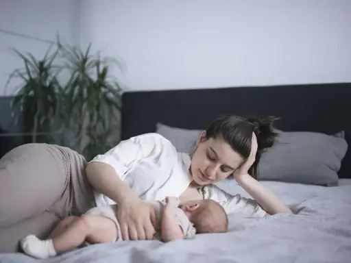Mama karmi na leżąco swoje dziecko na łóżku. Czuły moment bliskości i spokoju.