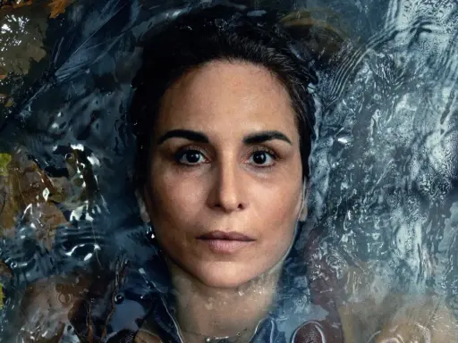 En kvinna med intensiv blick flyter i mörkt vatten, omgiven av höstlöv. En scen från veronica serie.
