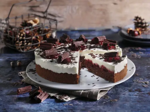 Schokoladen-Sahne-Torte mit Preiselbeeren und Schokostückchen, dekoriert mit Schokoraspeln. Ein Stück ist angeschnitten.