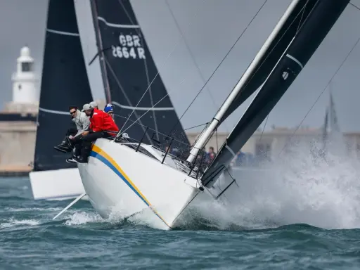Segelboote kämpfen bei der Admirals Cup Regatta um die Wette. Gischt spritzt, die Crew sitzt tief.