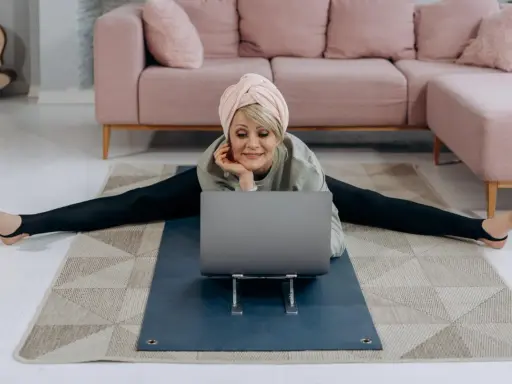 Kvinna i spagat framför laptop, med en rosa soffa i bakgrunden. Hon verkar lära sig om fosfor i kroppen.