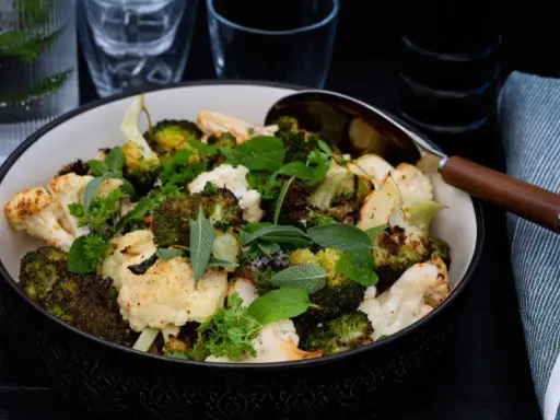 En skål med ugnsrostad blomkål och broccoli, toppad med färska örter. Perfekt som tillbehör till middagen.