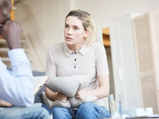 Kobieta trzyma poduszkę, rozmawiając z terapeutą. Czeka na zwolnienie od psychiatry, by móc wrócić do normalnego życia.