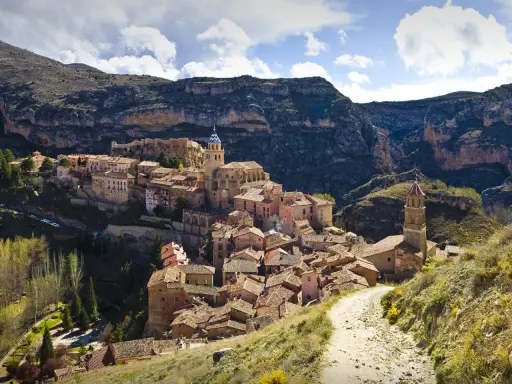 Malerisches Dorf Albarracín, Spanien, schmiegt sich an steile Felsen. Ein Weg führt durch grüne Hügel zum historischen Ortskern.