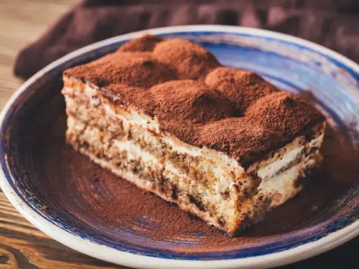 Pyszny kawałek tiramisu z mascarpone, posypany kakao, na talerzu. Idealny sprawdzony przepis na deser.