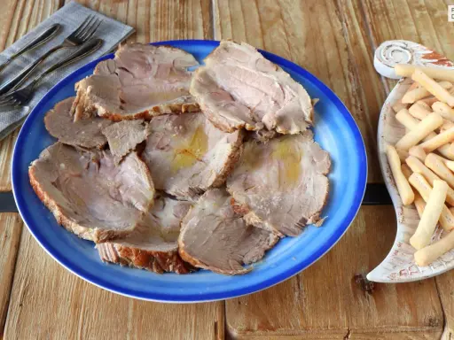 Plato azul con lonchas de jugosa carne mechada, servida con palitos de pan crujientes al lado.