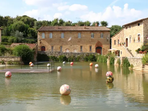 Paesini puglia con un laghetto pieno di sfere colorate, circondato da antichi edifici in pietra e vegetazione rigogliosa.