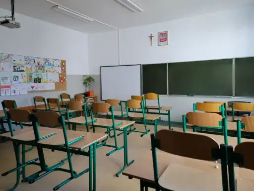 Pusta klasa szkolna z rzędami ławek i krzeseł. Na ścianie tablica, projektor i dziecięce rysunki. Wygląda na to, że **odwołane zajęcia w szkołach** sprawiły, że nikt dziś nie przyszedł.