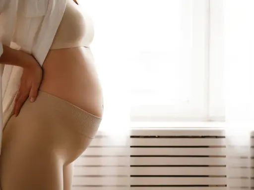 Donna incinta si tiene la schiena, forse per i crampi in gravidanza. Indossa una maglietta e una fascia di supporto.