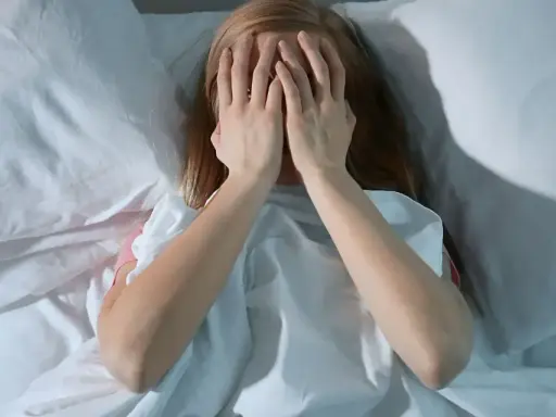 Nastolatka w łóżku, zakrywająca twarz dłońmi, symbolizuje bezsenność u nastolatków i jej przyczyny.