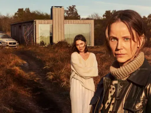 Två kvinnor står i ett torrt landskap framför ett modernt hus. En polisbil syns i bakgrunden. Sanningen serie.
