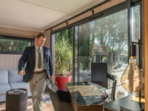 Un homme en costume entre dans un bureau lumineux avec vue sur un jardin. C'est la définition du home office : travailler depuis chez soi.