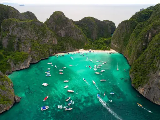 Maya Bay tętni życiem, pełna łodzi i turystów na piaszczystej plaży, otoczona stromymi, porośniętymi zielenią klifami.