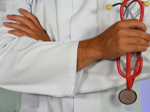 Lekarz w białym kitlu trzyma czerwony stetoskop. Dłonie skrzyżowane na piersi. Może to być pomocne przy diagnozowaniu zapalenia górnych dróg oddechowych.