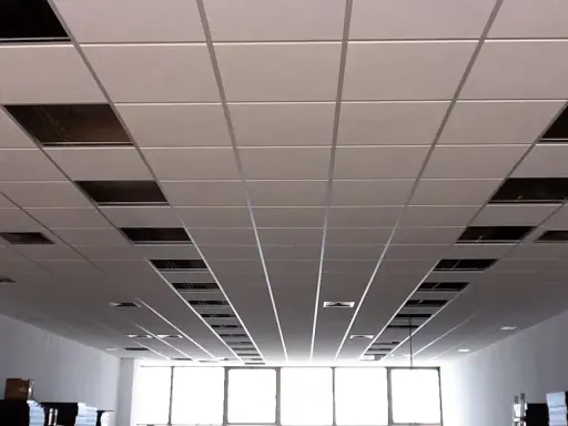 Instalación de un falso techo modular con paneles blancos y perfiles metálicos. Se aprecian huecos para iluminación o ventilación.