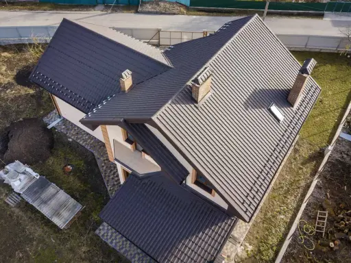 Nowy dach z ciemnej dachówki, z dwoma kominami i lukarną. Elewacja domu w odcieniach beżu i brązu. Facjata domu prezentuje się okazale.