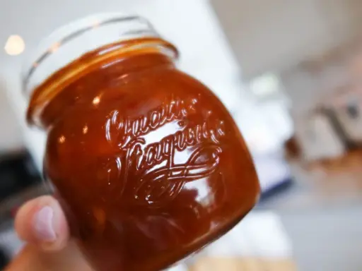 En hand håller ett glas med söt och syrlig rabarberchutney.