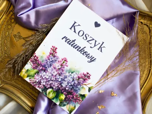 Eleganckie elementy zaproszenia: kartka z napisem "Koszyk ratunkowy", ozdobiona bukietem bzu, na tle fioletowej satyny i złotej ramki.
