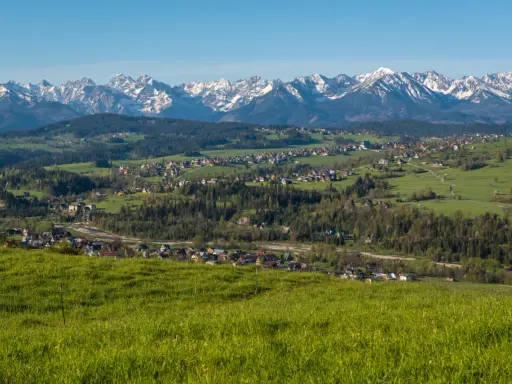 Widok na Tatry z zielonych wzgórz. W oddali widać zabudowania, które mogą być częścią trasy, ile km z Zakopanego do Bukowiny Tatrzańskiej.