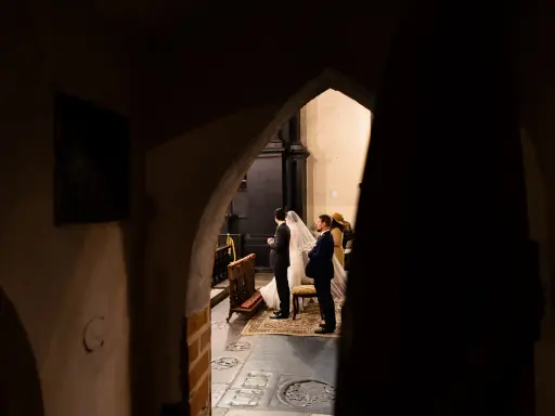 Ślub w kościele, para młoda i goście. Początkujący fotograf uchwycił ten magiczny moment zza ciemnego przejścia.