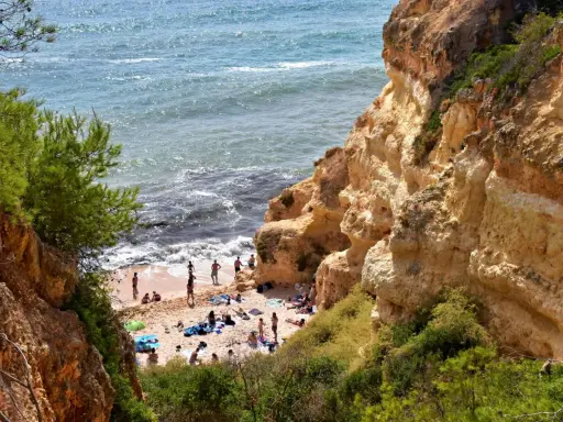 Sonnige Praia do Carvalho mit Felsen, grüner Vegetation und Badegästen am Meer.