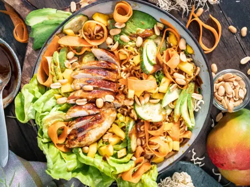 Ein bunter asiatischer Salat mit gegrilltem Hähnchen, Avocado, Mango, Karottenstreifen und Erdnüssen.
