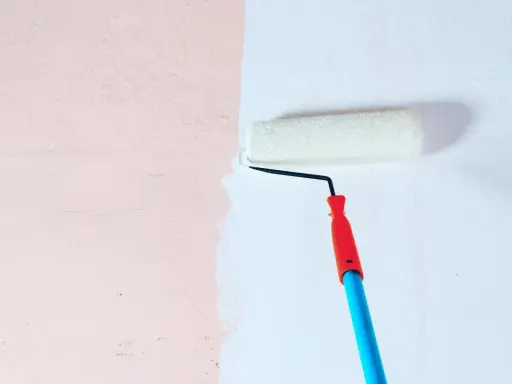 Malowanie ściany wałkiem. Decyzja: farba ceramiczna czy lateksowa? Jasnoróżowa ściana zyskuje białe wykończenie.