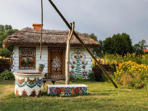 Kolorowy dom i studnia w malowniczej wsi Zalipie, ozdobione ludowymi wzorami kwiatowymi.