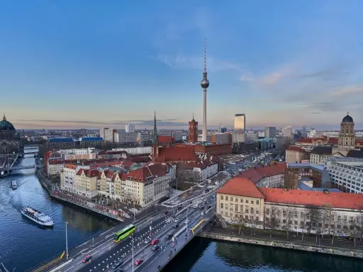 Ampio panorama berlino con la Torre della Televisione, il Duomo e il fiume Sprea. Traffico e barche animano la scena urbana.