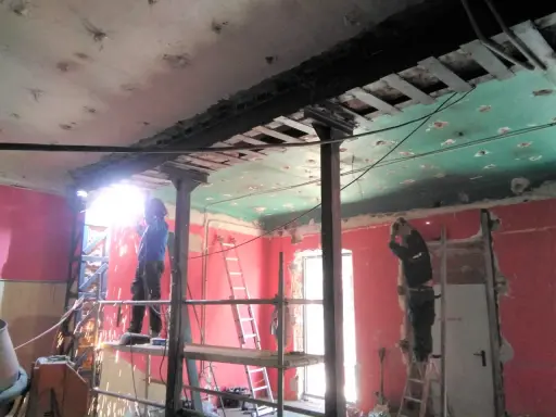 Trabajadores realizan el apeo de muro de carga con soportes metálicos y soldadura. El techo está en proceso de demolición.