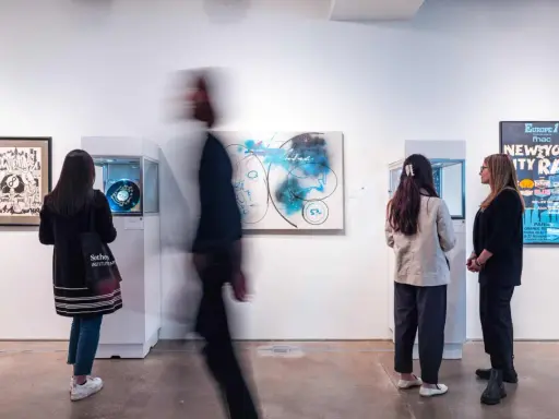 Visitors observe abstract art and a "New York City Rap" poster at a gallery exhibition.