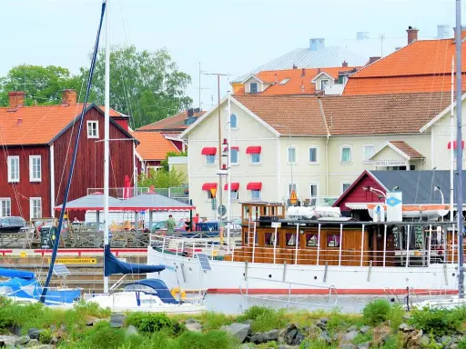 Båtar vid kajen framför hotell Vänerport i Mariestad. Röda och gula hus med tegeltak.
