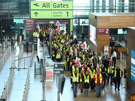 Tłum pracowników w kamizelkach odblaskowych z flagami maszeruje przez lotnisko w Berlinie, protestując. Strajk lotnisko Berlin zakłóca ruch.