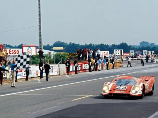 Ein roter Porsche Rennwagen mit der Startnummer 23 überquert die Ziellinie, während eine karierte Flagge geschwenkt wird.