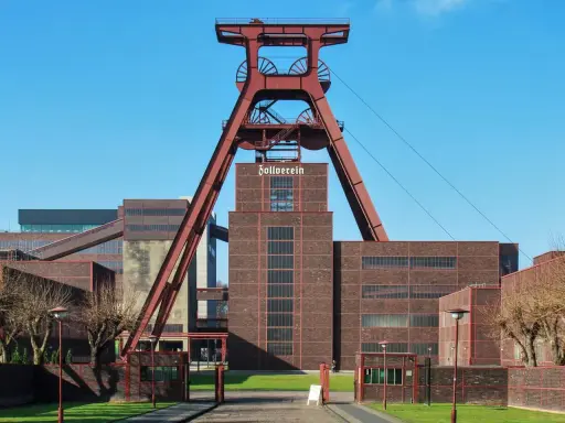 Industrielles Erbe mit rotem Förderturm und Backsteingebäuden. Die Zeche Zollverein strahlt eine starke, urbane Energie aus.