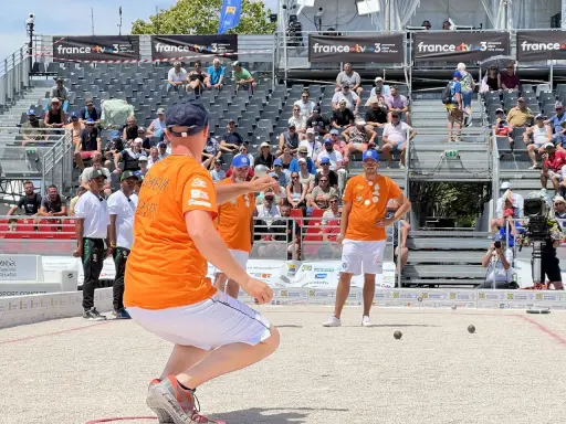Joueur de pétanque concentré, cherchant à faire le vide dans sa tête avant de lancer la boule. Le public est installé dans les gradins derrière lui.