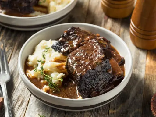 Un succulento brasato di manzo servito con purè di patate e guarnito con timo fresco.