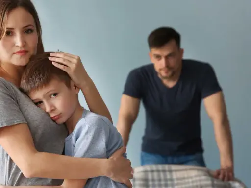 Smutna kobieta tuli syna, podczas gdy partner patrzy z dystansu. Trudno jej zaakceptować dziecko partnera.