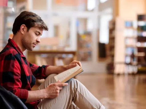Mężczyzna w kratę czyta książkę w bibliotece.