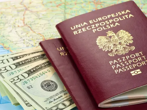 Dwa polskie paszporty, stos banknotów dolarowych i mapa świata.