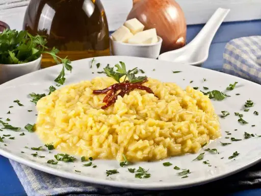 Aksamitne risotto alla milanese, ozdobione suszonymi papryczkami i natką pietruszki, prezentuje się apetycznie na białym talerzu.