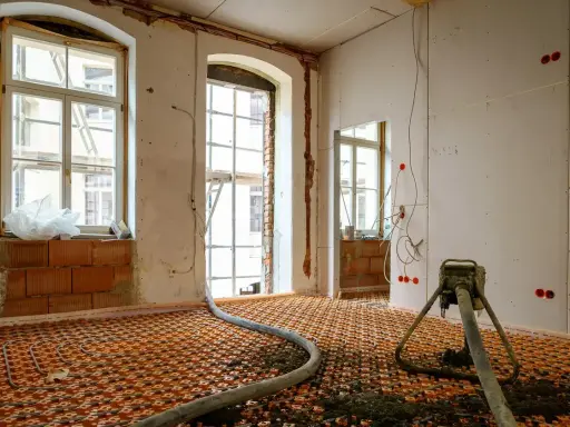 Installation d'un chauffage au sol ancienne génération, avec tuyaux orange et une machine de projection de chape.