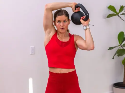 Frau trainiert mit einer Kettlebell deutsch, hebt sie über den Kopf.