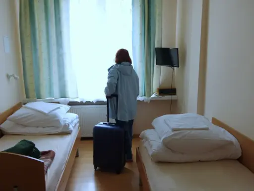 Kobieta z walizką przy oknie, gotowa by dowiedzieć się, jak wyjechać do sanatorium. Pokój z dwoma łóżkami.