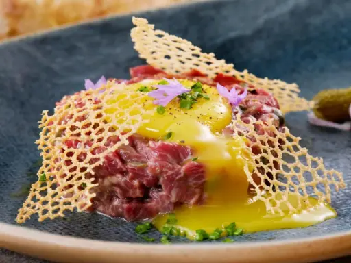 Delicioso steak tartar con huevo crudo, crujiente de queso y pepinillos. Una receta para disfrutar.