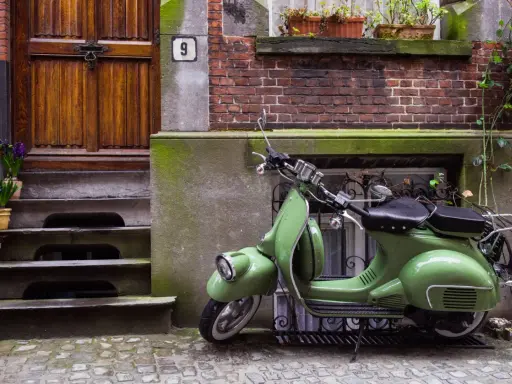 Zielony skuter, klasyk, czeka na właściciela. Parkowanie motocykla na chodniku przed drzwiami z numerem 9.