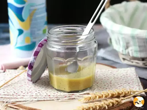 Un bocal de vinaigrette maison, prêt à assaisonner une salade fraîche. Une cuillère repose dans le mélange jaune pâle.